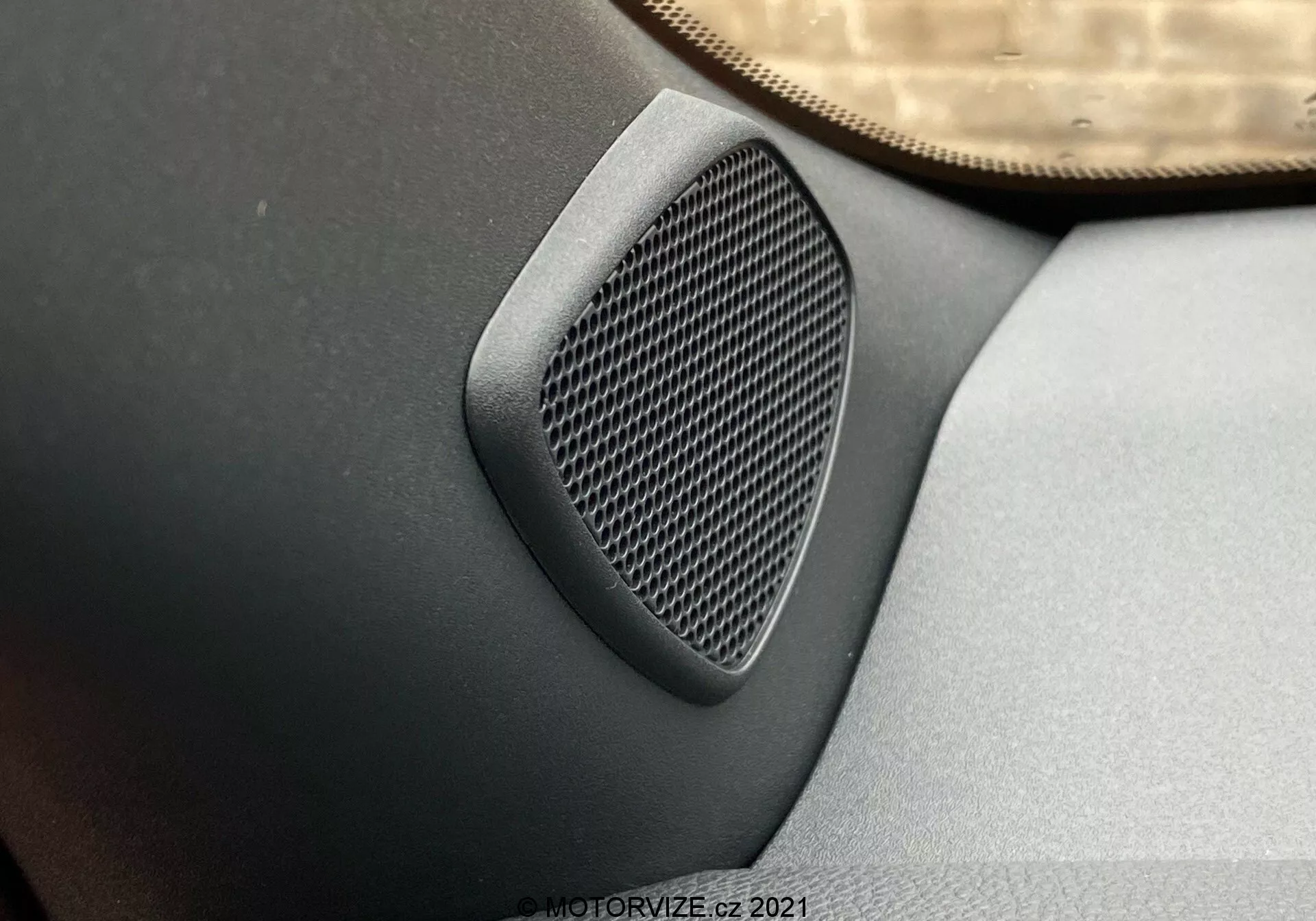 Vista de cerca de un altavoz de coche en el panel de la puerta con un patrón geométrico en la rejilla, integrado en gris oscuro o negro en el panel, tomada desde un ángulo elevado destacando la textura del altavoz y la calidad del audio en un Toyota Yaris 2020.