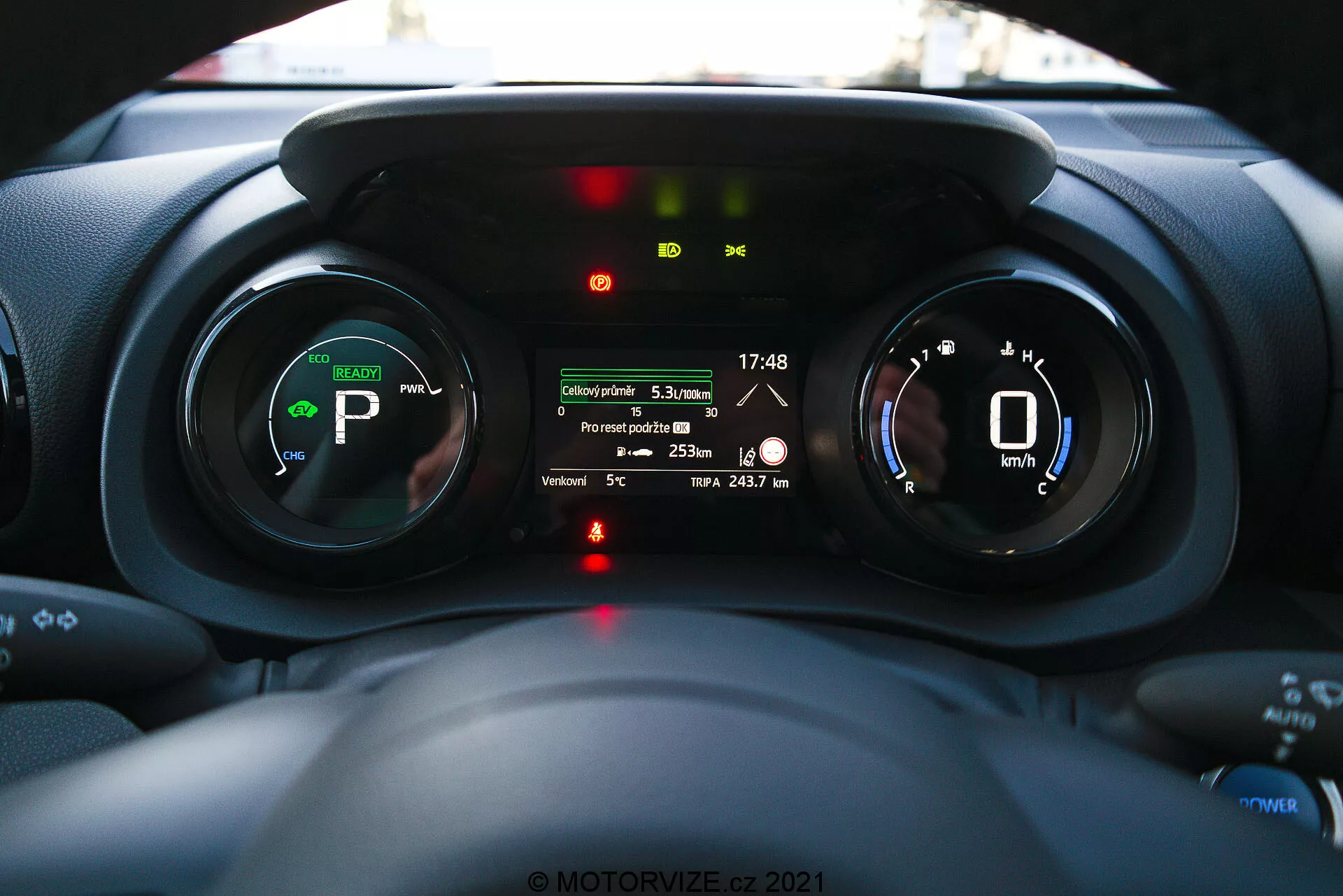 Vista interior del tablero de instrumentos del Toyota Yaris 2020 enfocado en el panel de instrumentos, tomada desde la perspectiva del conductor mostrando indicadores digitales, indicadores de vehículo eléctrico o híbrido y una pantalla de información múltiple con características como la distancia del viaje, temperatura exterior y rango de la batería.