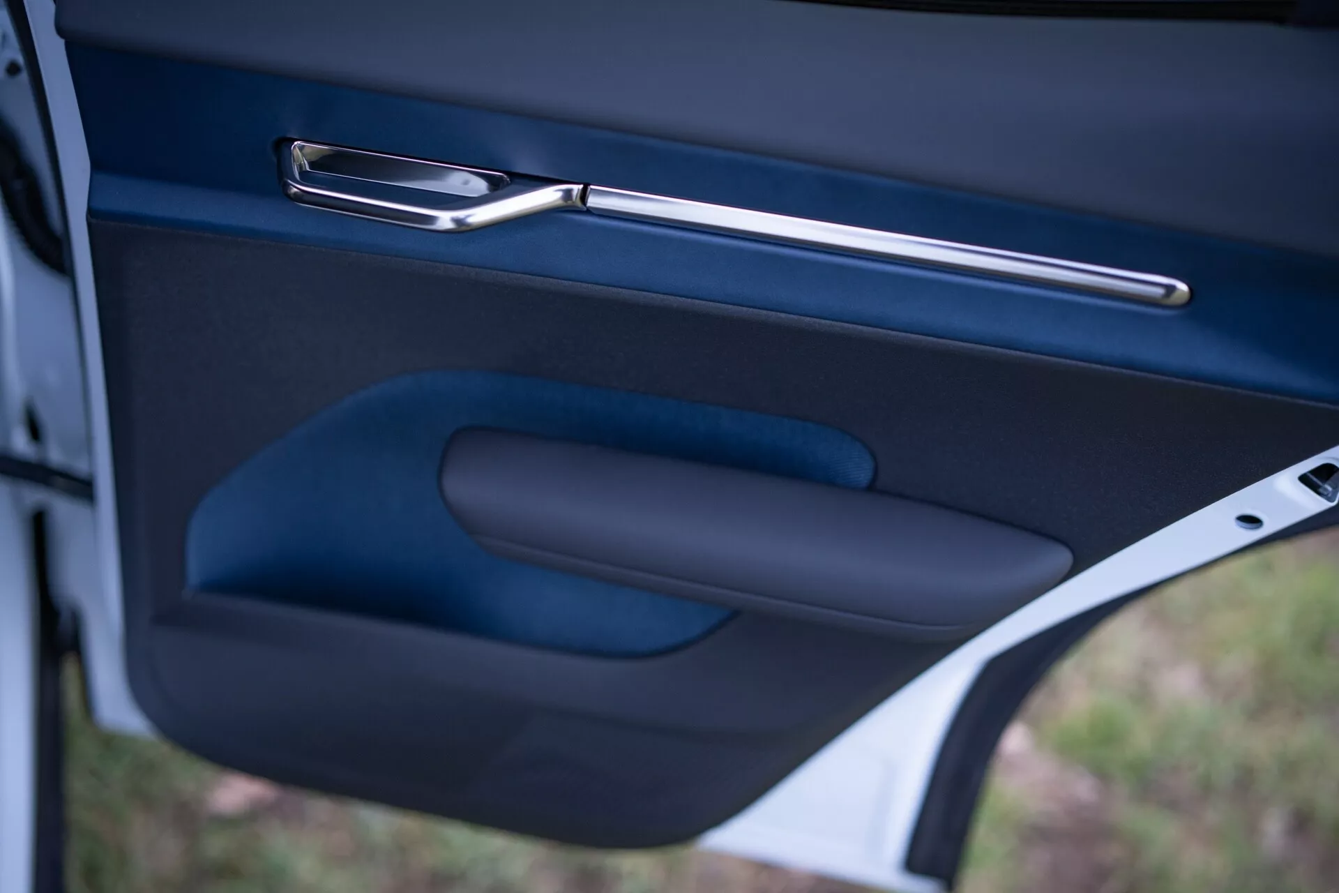 Primer plano del interior de la puerta del Volvo EX30 2024, mostrando la elegante manija metálica de la puerta, el apoyabrazos ergonómico y el bolsillo de almacenamiento en un acabado oscuro de alta calidad