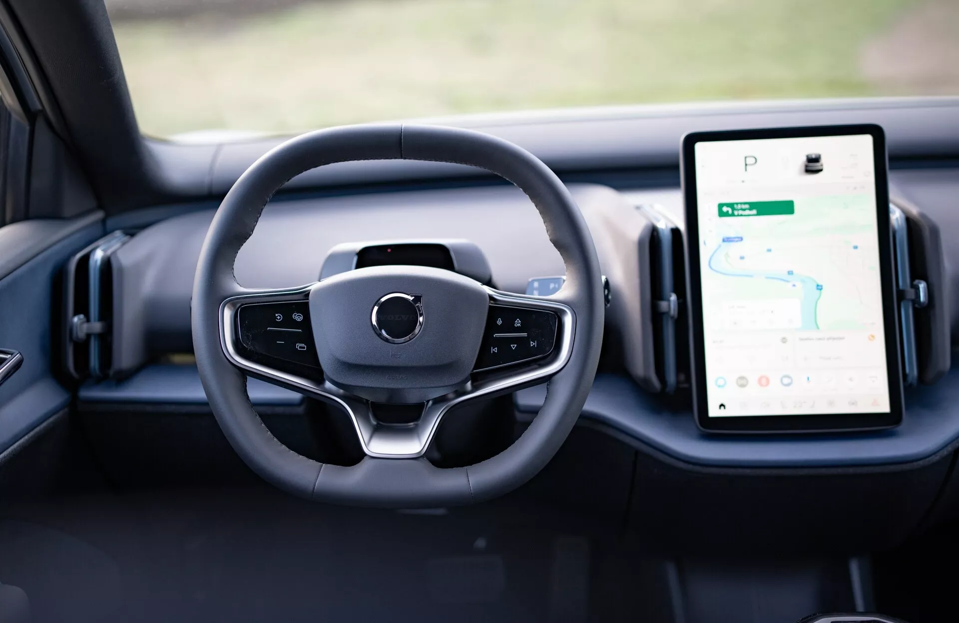 Vista interior del Volvo EX30 2024 mostrando el diseño moderno del volante y los diales digitales en el tablero, incluido el sistema de infoentretenimiento táctil orientado verticalmente con GPS.