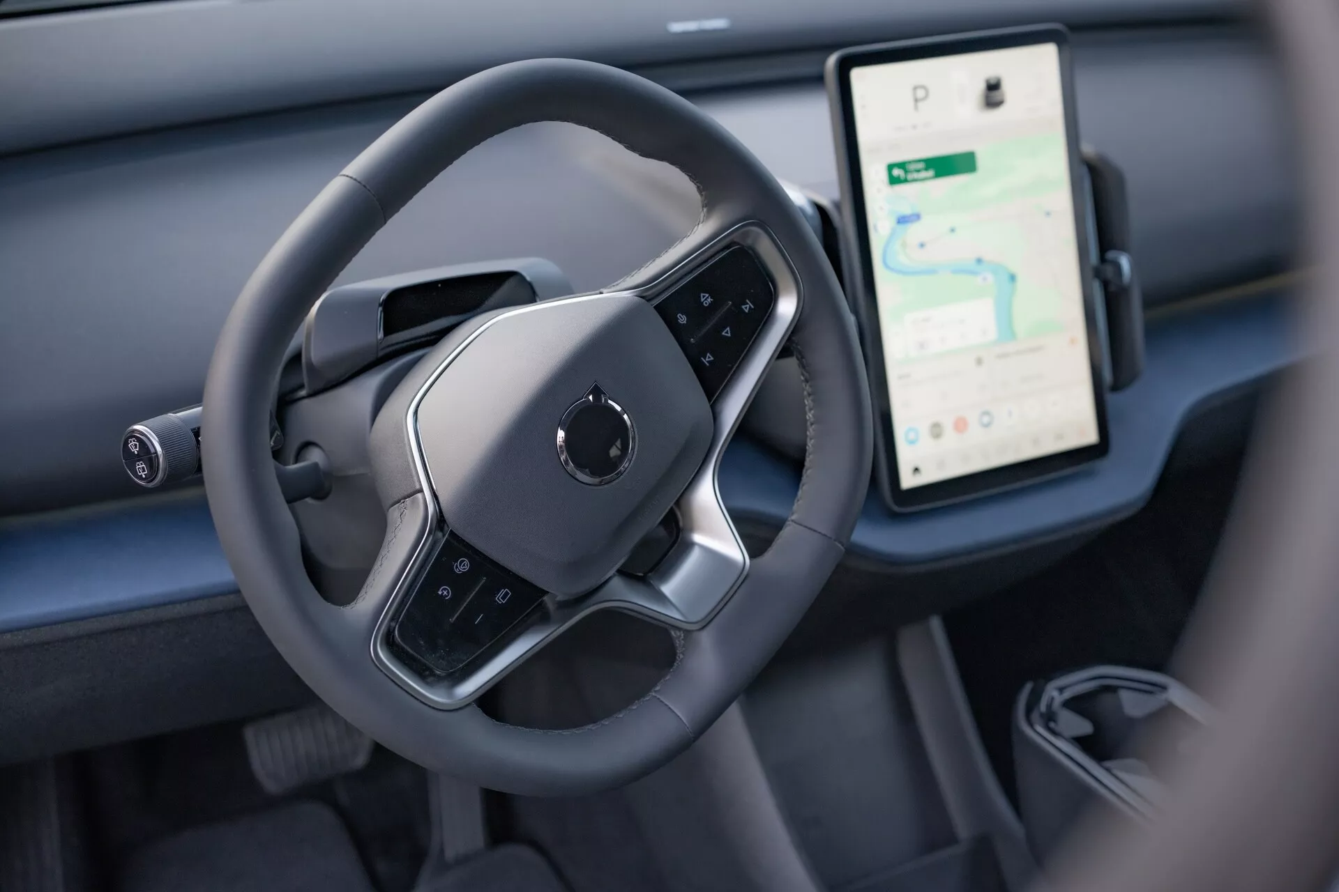 Vista interior del Volvo EX30 2024 destacando el área de control del conductor con un volante moderno de fondo plano y una gran pantalla táctil vertical para navegación y medios en el tablero