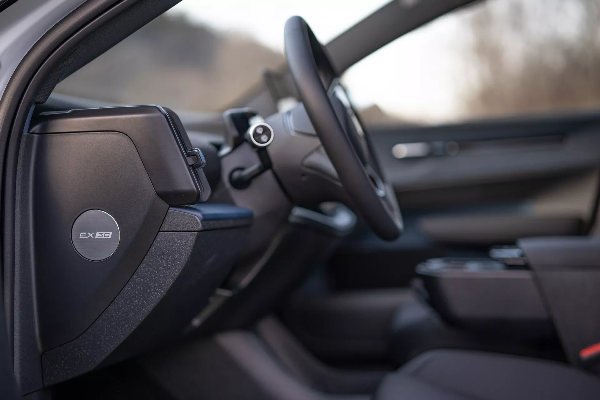 Vista interior del Volvo EX30 2024 enfocada en el lado del conductor con diseño de asiento deportivo o premium detallado, sistema de audio Harman Kardon en el pilar B, volante multifunción y pistas de un avanzado sistema de infoentretenimiento y diseño del panel de la puerta del pasajero