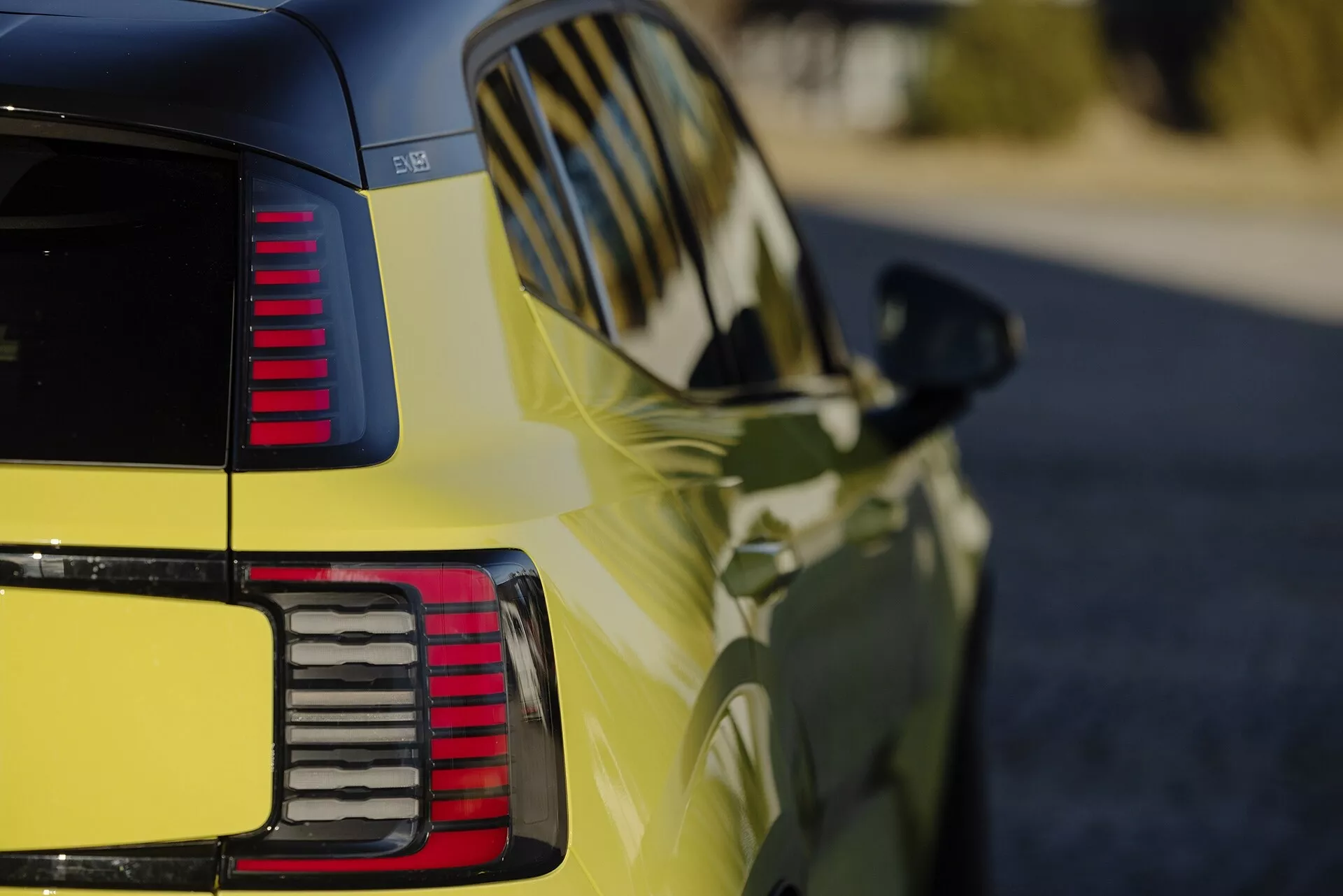Vista detallada de la cuarta trasera de un Volvo EX30 2024 en amarillo vibrante, mostrando el acabado brillante, luces traseras LED segmentadas, líneas de diseño aerodinámico y señales de giro integradas en el espejo lateral