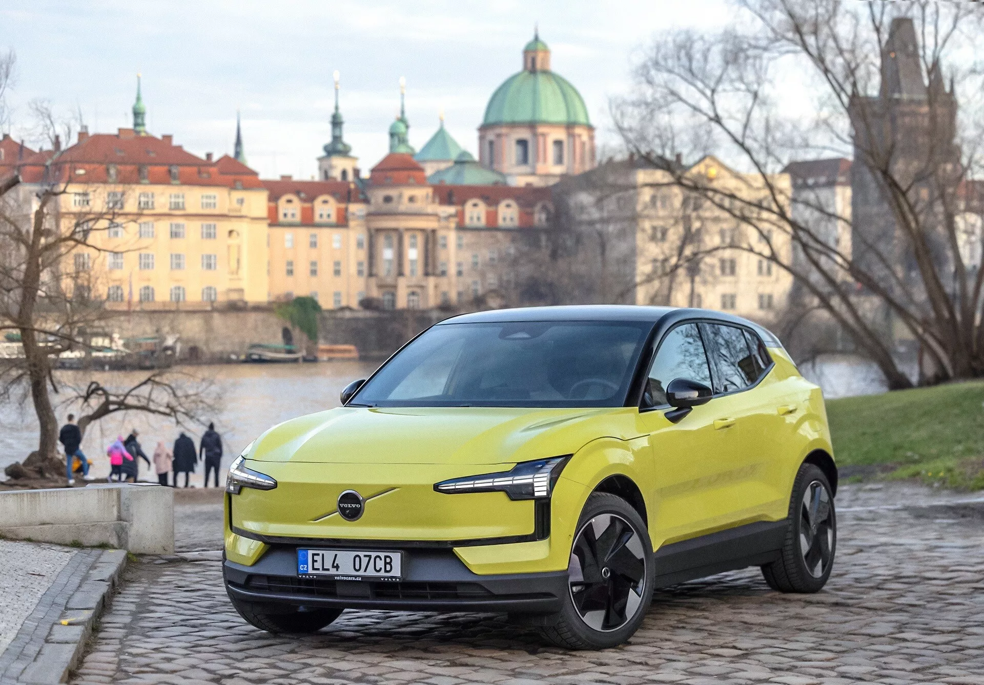 Volvo EX30 2024 en verde lima, vista frontal de tres cuartos en adoquines, con faros LED modernos y características de diseño eléctrico, fondo urbano europeo