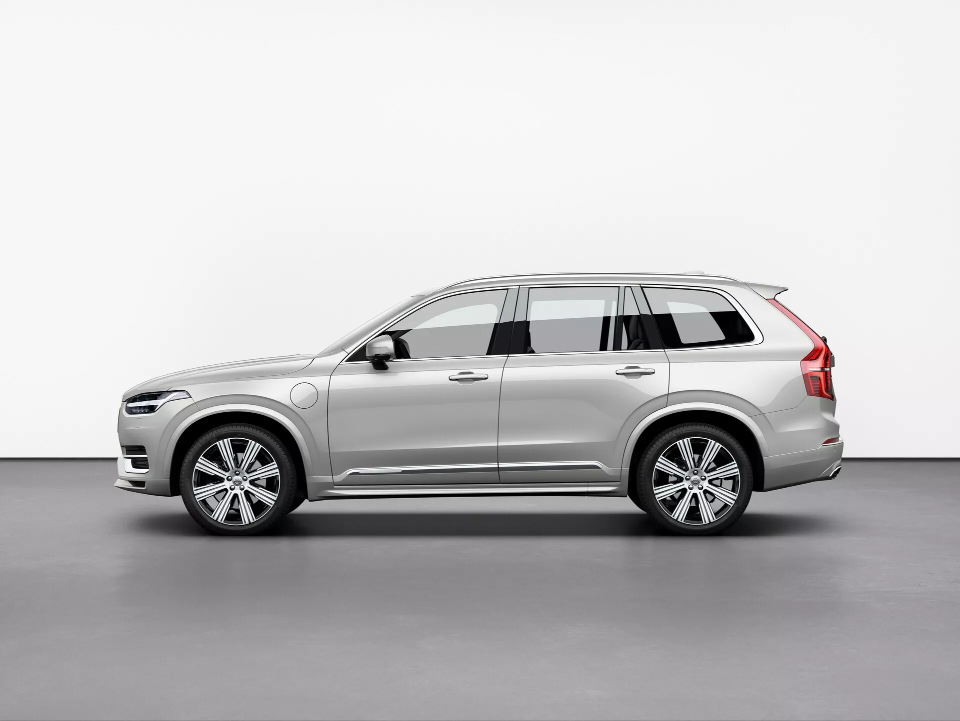 Imagen del SUV Volvo XC90 2015, fotografiado desde una vista de tres cuartos en un ligero ángulo. Esta vista destaca los perfiles delantero y lateral, mostrando el diseño elegante y moderno del coche, los faros LED intrincados, la parrilla frontal parcialmente visible, llantas de aleación de aluminio de varios radios, espejos laterales con señales de giro integradas, rieles en el techo, líneas de carácter dinámico, la pintura y el color del coche. La suave iluminación en el entorno del estudio refleja con precisión los contornos y detalles superficiales del vehículo.