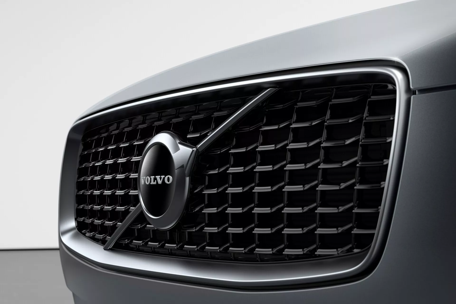 Vista de cerca de la parrilla frontal de un Volvo XC90 2015 (2da generación), que muestra el diseño detallado y el prominente emblema de la marca Volvo. La parrilla presenta listones verticales y un contorno cromado, destacando el lujo y la estética moderna.