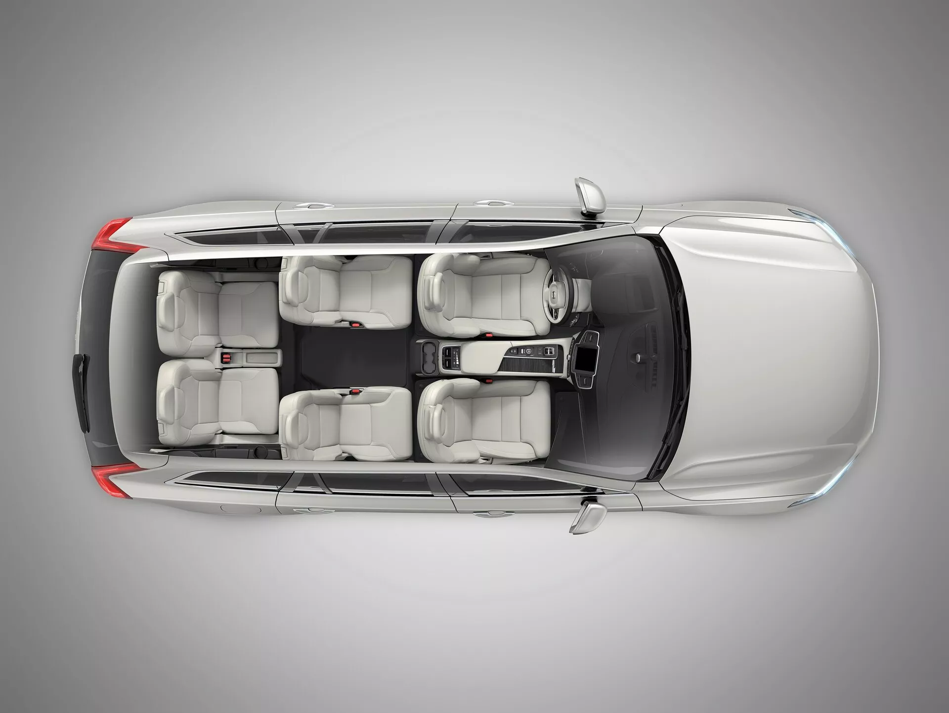 Vista desde arriba del Volvo XC90 2015 (2ª generación) que muestra su exterior gris metálico plateado, carrocería SUV de cuatro puertas, ventanas con protección UV tintada, interior con capacidad para siete asientos con asientos en gris claro, y llantas de aleación. La imagen destaca características inferidas como ADAS, seguridad del vehículo, sistema de infoentretenimiento, control de clima multizona, entrada sin llave y sistemas de asistencia al aparcamiento, con iluminación de estudio asegurando un claro enfoque en el diseño detallado del coche.