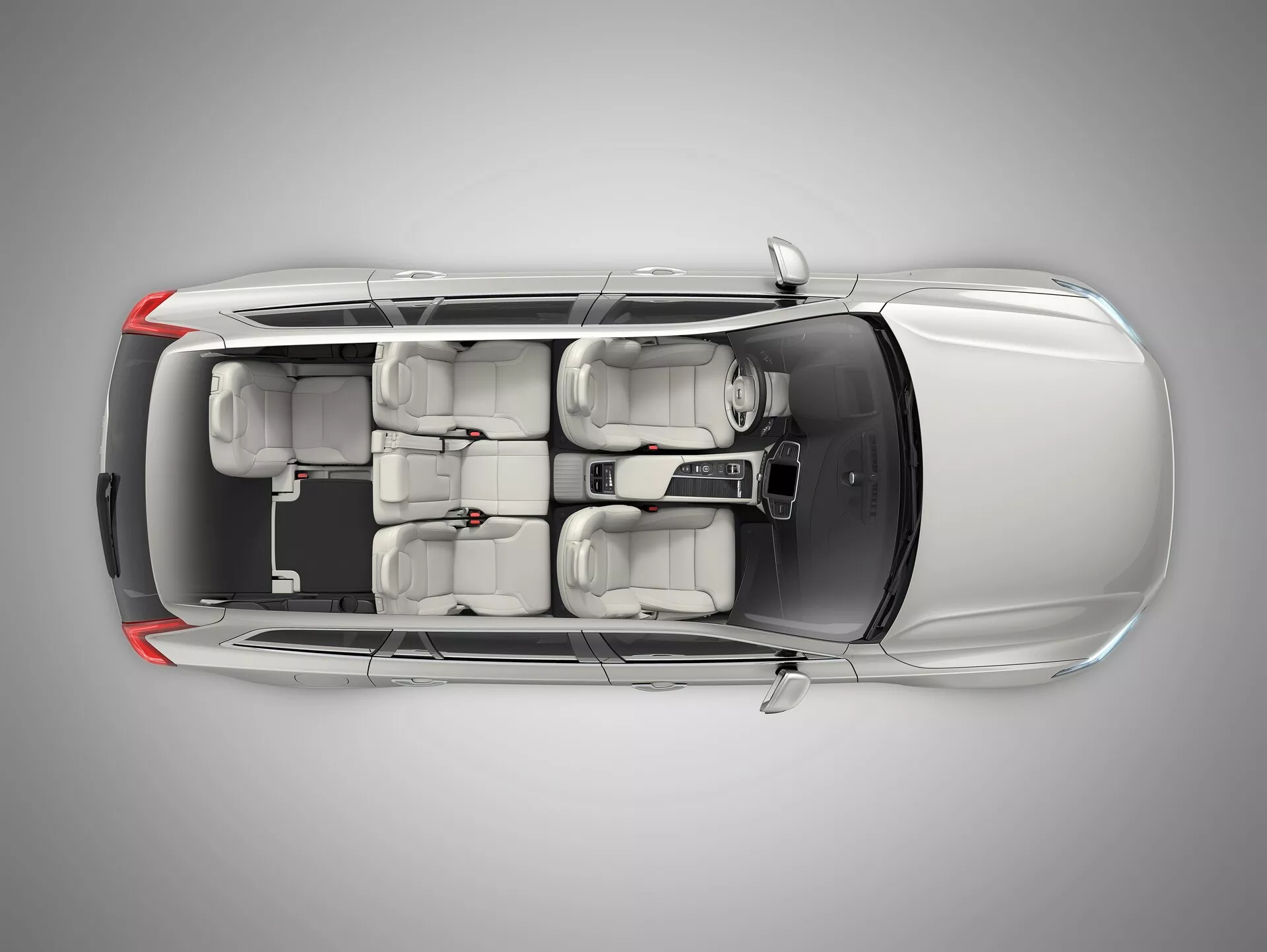 Vista aérea cenital de un bien mantenido sedán plateado claro Volvo XC90 de segunda generación del 2015. La imagen captura toda la longitud y anchura del coche, mostrando todo el techo, la carrocería y los alrededores. Todas las ventanas y puertas están cerradas con manillas de puertas integradas suavemente y espejos laterales retráctiles. El techo no tiene techo solar y el acabado de la pintura es uniformemente reflectante. El interior es visible a través del techo transparente, destacando la tapicería beige o gris claro, dos filas de asientos con reposacabezas y neumáticos estándar. La forma de los alojamientos de las luces traseras y delanteras es visible pero no detallada.
