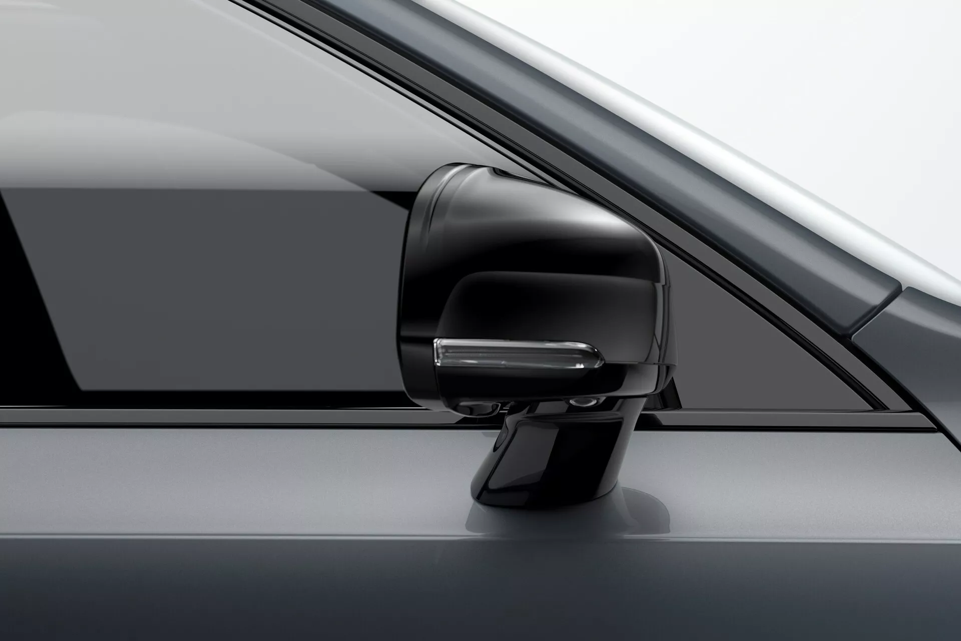 Vista de cerca del conjunto del espejo lateral del lado del conductor en un Volvo XC90 2015 (2.ª generación). La imagen resalta el diseño aerodinámico moderno con una señal de giro integrada, posiblemente parte del sistema avanzado de asistencia al conductor, y una carcasa con el mismo color. Se puede ver una vista parcial del pilar A, la ventana lateral y el panel de la puerta. La fotografía está tomada desde un ángulo ligeramente frontal, mostrando el aspecto monocromático premium del vehículo.