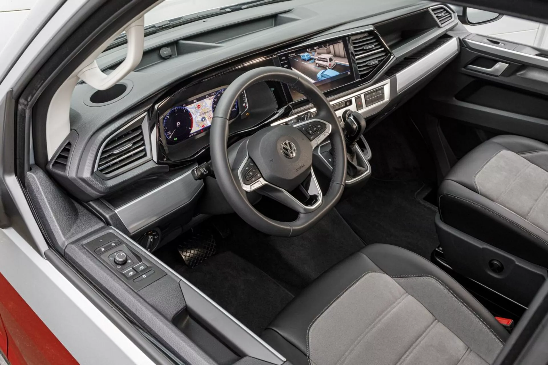 Vista elevada del interior del Volkswagen Nutzfahrzeuge Transporter 2019 (T6.1 California) mostrando el área del conductor con tablero digital, pantalla táctil multimedia y asientos tapizados en dos tonos