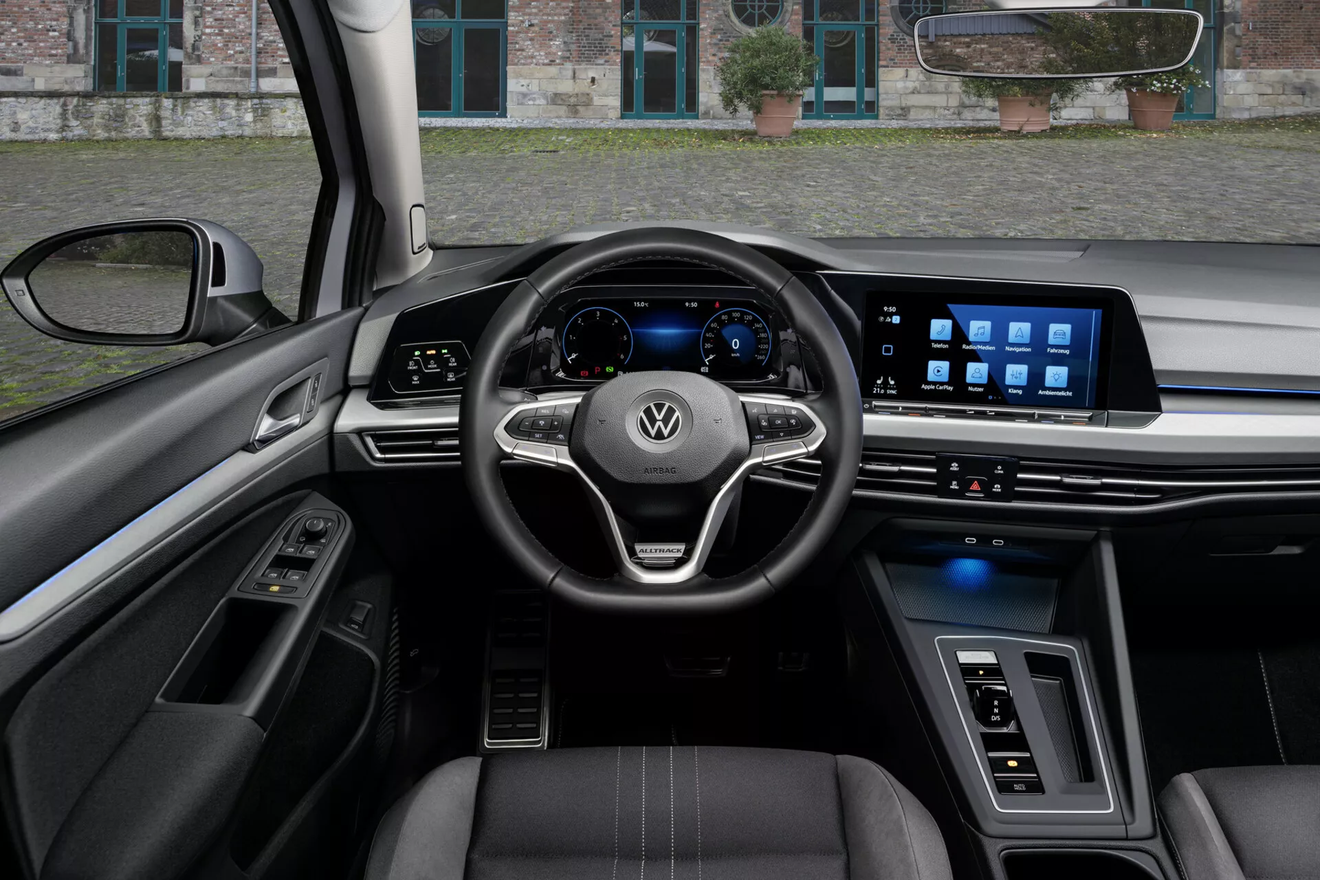 Vista interior de un VW Golf Alltrack 2017 desde la perspectiva del conductor, mostrando un volante de tres radios con controles montados y el logo de Volkswagen, un cuadro de instrumentos digital y un amplio sistema de infoentretenimiento táctil en el tablero, destacado por características tecnológicas avanzadas, asientos tapizados en cuero con costuras en contraste, y una mezcla de materiales de lujo e iluminación ambiental.