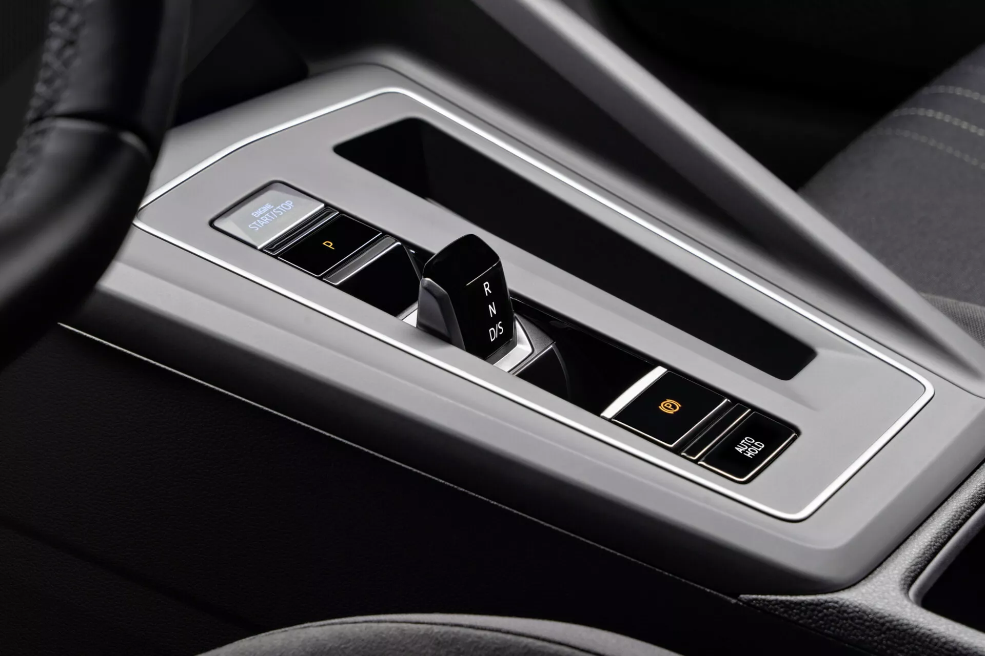 Primer plano del centro de mando del VW Golf Alltrack 2017, destacando la palanca de cambios de la transmisión automática enmarcada en metal brillante con una pantalla electrónica, rodeada de cuero negro o cuero sintético y presentando indicadores de marcha, modo deportivo y botones para asistencias avanzadas al conductor.
