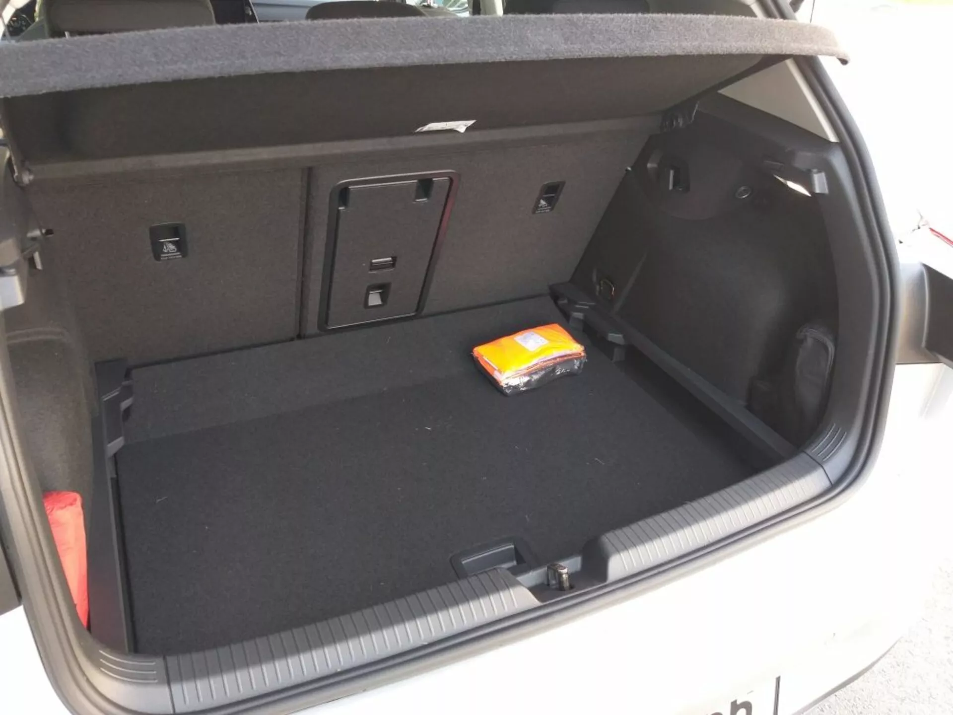 Compartimento del maletero del Volkswagen Golf GTD 2017 mostrando la distribución y diseño completos con forro de alfombra negra plana, área principal de carga vacía con un pequeño paquete de toallitas húmedas, compartimentos laterales para artículos pequeños o equipo, acceso a asientos traseros abatibles para espacio extendido, enchufe de 12V en el lado derecho, luz integrada en el maletero y detalles que sugieren una operación de apertura/cierre manual