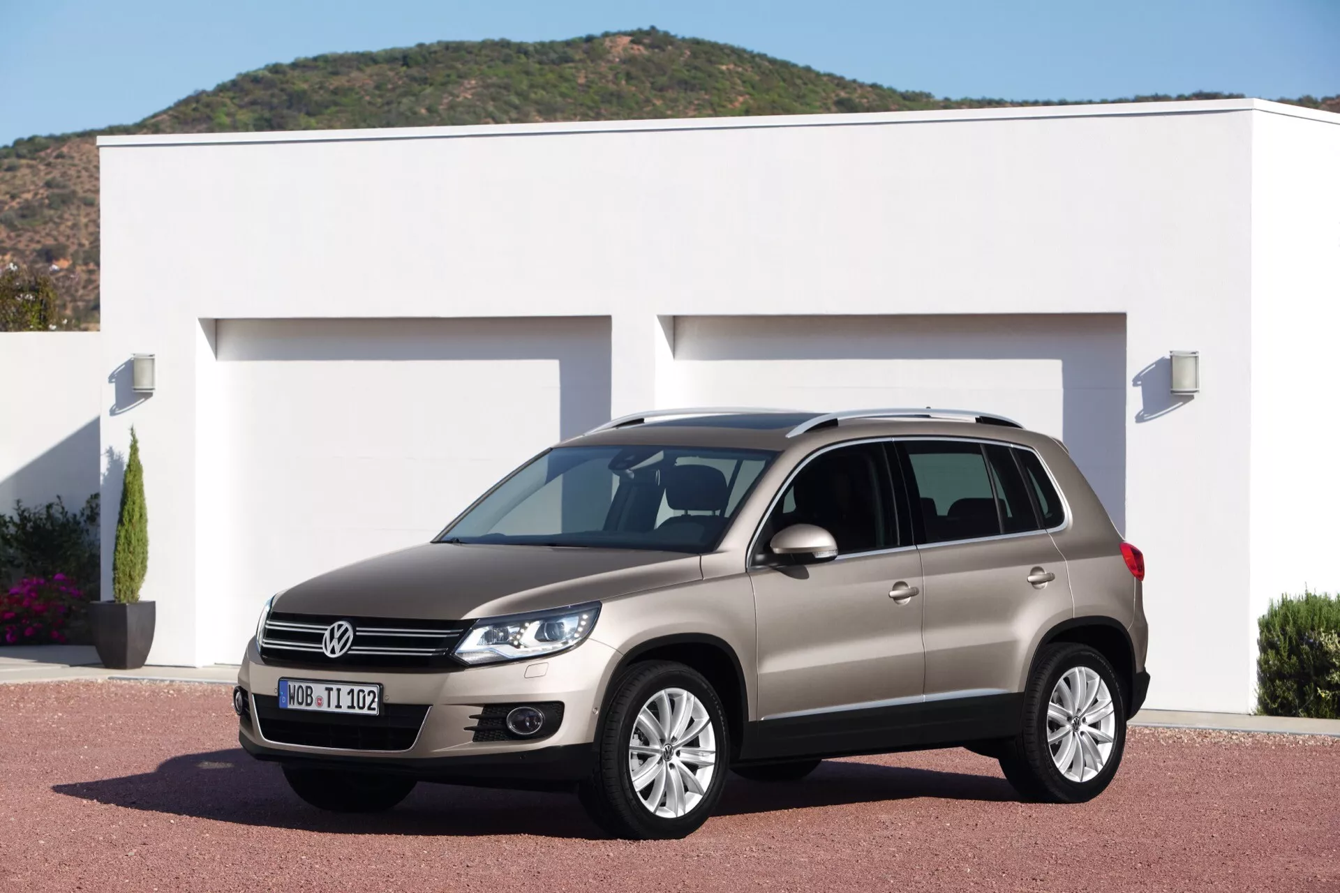 Volkswagen Tiguan de 2007 estacionado en la entrada de una casa moderna, mostrando sus ruedas de aleación, faros distintivos, luces diurnas y barras en el techo, bajo la luz brillante del día