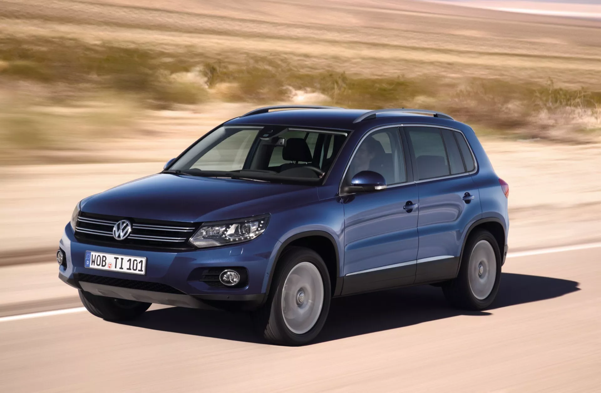 Volkswagen Tiguan del 2007 en movimiento, capturado desde un ángulo frontal tres cuartos mostrando el lado del conductor, con características como ruedas de aleación, barras de techo, faros encendidos, contra un telón de fondo de un terreno árido y plano